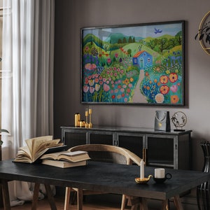 May include: A colorful painting of a blue house in a field of flowers. The house has a white door and a red roof. The flowers are in shades of pink, red, yellow, and orange. The painting is framed in black and hangs on a gray wall.