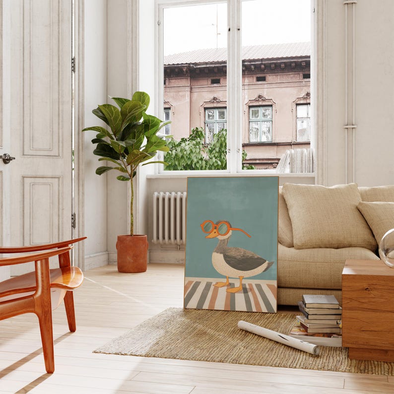 May include: A framed art print featuring a whimsical illustration of a goose wearing orange glasses. The goose stands on a striped surface against a teal background. The artwork is displayed in a bright, airy room with a sofa and a potted plant.