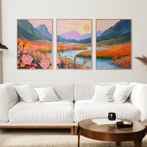 Könnte beinhalten: Drei gerahmte Landschaftsbilder mit einer Bergkette, einem Fluss und einem Feld mit orangefarbenen und rosa Blüten. Die Bilder hängen an einer weißen Wand über einem weißen Sofa.