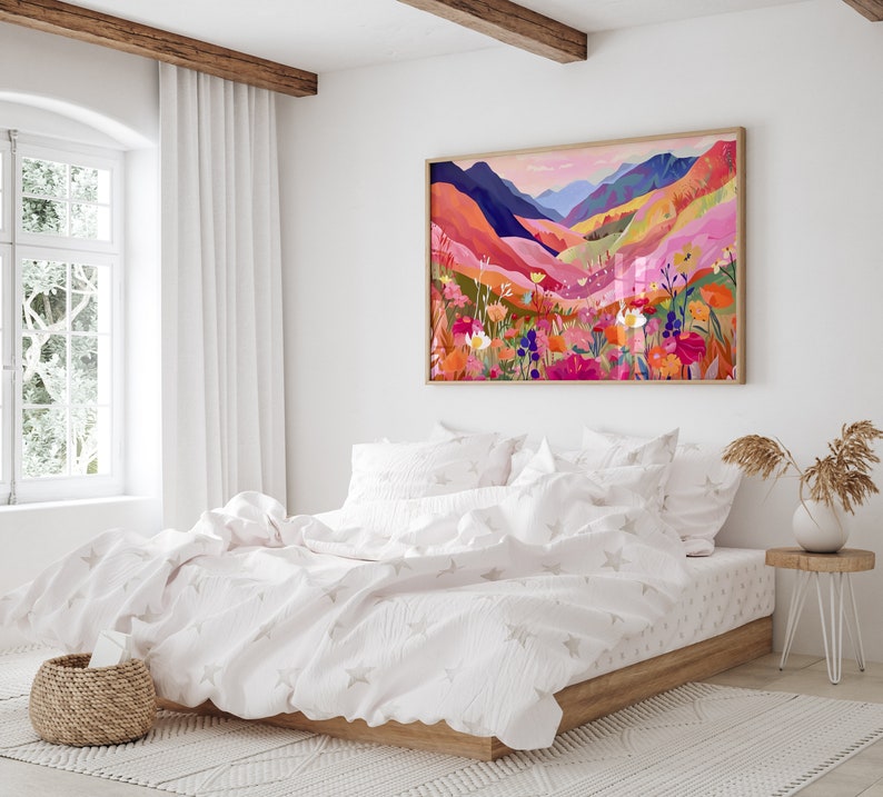 K&ouml;nnte beinhalten: Ein wei&szlig;es Bett mit einem rosa-wei&szlig;en gemusterten Bettbezug und einem gerahmten Druck einer farbenfrohen Landschaft mit Bergen und Blumen. Der Druck h&auml;ngt an einer wei&szlig;en Wand &uuml;ber dem Bett.