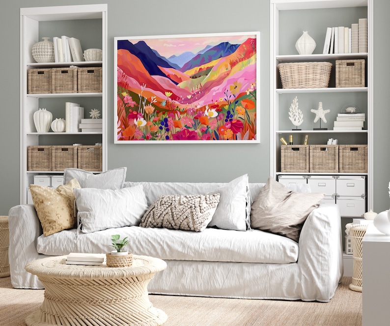 K&ouml;nnte beinhalten: Ein wei&szlig;es Sofa mit Kissen steht vor einem wei&szlig;en B&uuml;cherregal mit Weidenk&ouml;rben und einem gerahmten Druck eines farbenfrohen Landschaftsbildes mit Bergen und Blumen.
