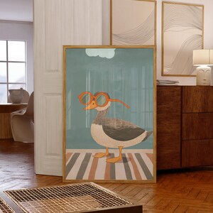 May include: A framed art print featuring a whimsical illustration of a duck wearing orange glasses. The duck is depicted in shades of gray, white, and brown, standing on a striped rug. The background is a muted teal color, with a light blue cloud.