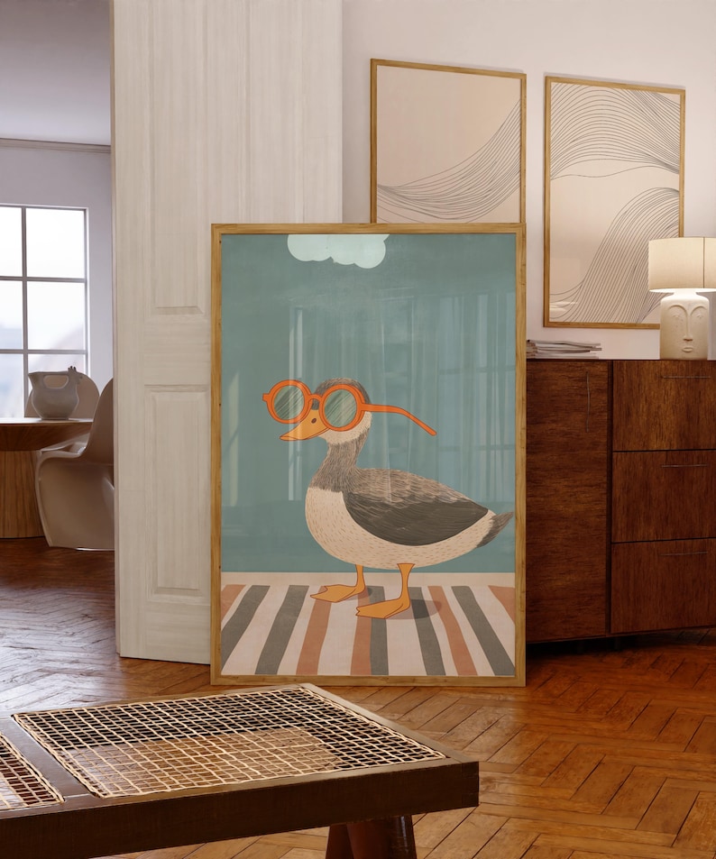 May include: A framed art print featuring a whimsical illustration of a duck wearing orange glasses. The duck is depicted in shades of gray, white, and brown, standing on a striped rug. The background is a muted teal color, with a light blue cloud.