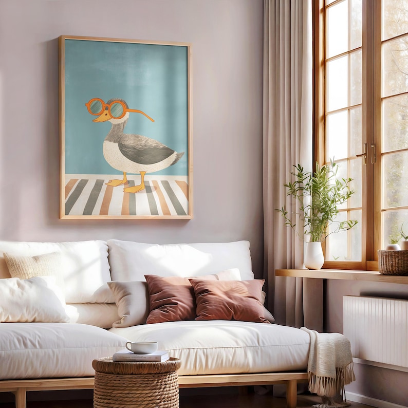 May include: A framed art print featuring a whimsical illustration of a duck wearing orange sunglasses. The duck is depicted in shades of gray, white, and yellow, standing on a striped surface against a light blue background. The artwork is in a wooden frame.