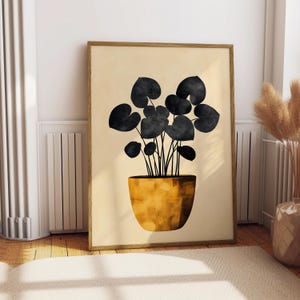 May include: A framed wall art print featuring a stylized illustration of a potted plant with dark black heart-shaped leaves. The plant is housed in a textured, golden-yellow pot, set against a solid, light beige background within a wooden frame.