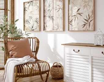 May include: A wicker chair with a brown cushion and a white throw blanket sits in a room with a white cabinet and three framed prints with botanical illustrations.