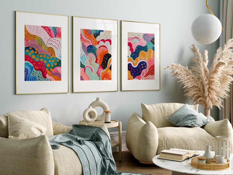 May include: Three framed abstract paintings with colorful, swirling patterns in shades of pink, blue, green, yellow, and orange. The paintings are hung on a light blue wall in a living room setting.
