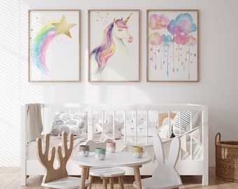 Puede incluir: Una cuna blanca con decoración de guardería temática de arcoíris, unicornio y nubes. La cuna está decorada con almohadas coloridas y una manta blanca. Hay una mesa pequeña y sillas en primer plano.