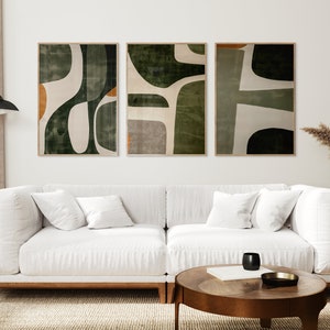 Op de afbeelding: Drie abstracte kunstprints in een woonkamer. De prints hebben een geometrisch ontwerp in de kleuren groen, wit en bruin. De prints zijn ingelijst in een natuurlijke houten lijst.