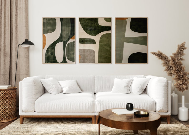 Op de afbeelding: Drie abstracte kunstprints in een woonkamer. De prints hebben een geometrisch ontwerp in de kleuren groen, wit en bruin. De prints zijn ingelijst in een natuurlijke houten lijst.
