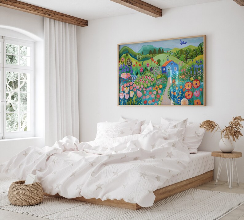 May include: A white bed with a white duvet cover and a white throw pillow. The bed is in a bedroom with a large window and a painting of a blue house in a field of flowers hanging on the wall.