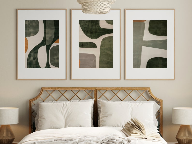 Op de afbeelding: Drie ingelijste abstracte kunstprints met een groen, wit en oranje kleurenschema. De prints hangen aan een muur boven een houten hoofdeinde.