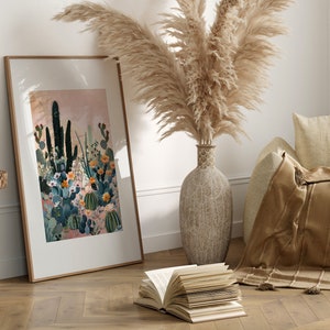 Pu&ograve; includere: Una stampa incorniciata di un paesaggio desertico con cactus e fiori in tonalit&agrave; di verde, rosa e arancio. La stampa &egrave; appesa a una parete bianca accanto a un vaso di erba della pampa secca.