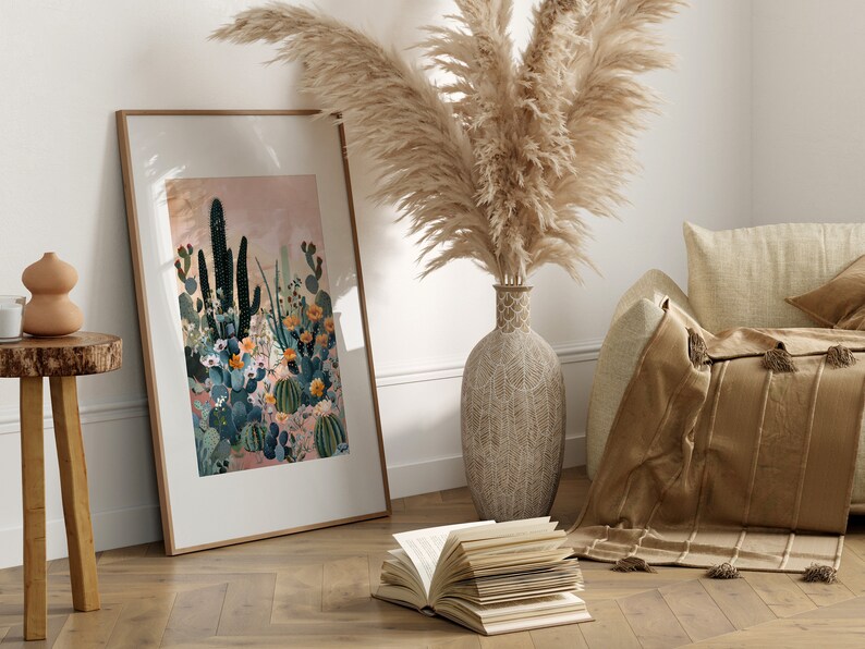 Pu&ograve; includere: Una stampa incorniciata di un paesaggio desertico con cactus e fiori in tonalit&agrave; di verde, rosa e arancio. La stampa &egrave; appesa a una parete bianca accanto a un vaso di erba della pampa secca.
