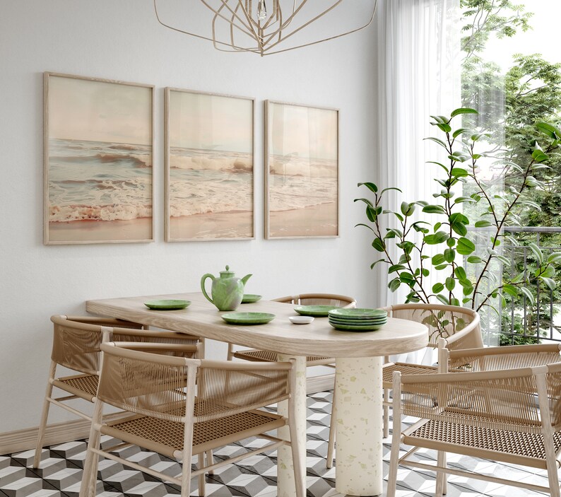 May include: A dining room with a wooden table and six woven chairs. The table has a green teapot and four plates on it. Three framed pictures of ocean waves hang on the wall. A potted plant is in the corner of the room.