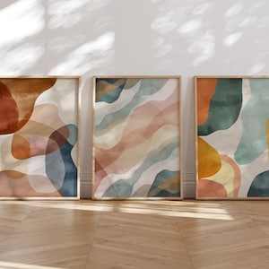 Puede incluir: Tres impresiones de arte abstracto en marcos de madera. Las impresiones presentan un estilo acuarela con formas superpuestas en tonos de azul, verde, naranja y rosa.