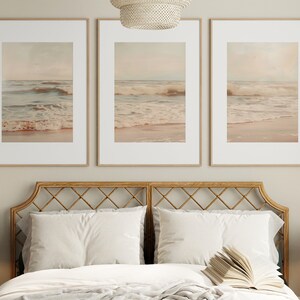 May include: Three framed prints of a beach scene with waves crashing on the shore. The prints are in a light beige color scheme and are hung above a bed with a woven headboard.