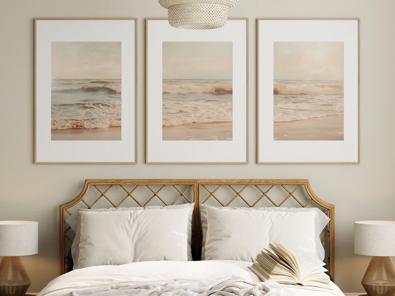 May include: Three framed prints of a beach scene with waves crashing on the shore. The prints are in a light beige color scheme and are hung above a bed with a woven headboard.