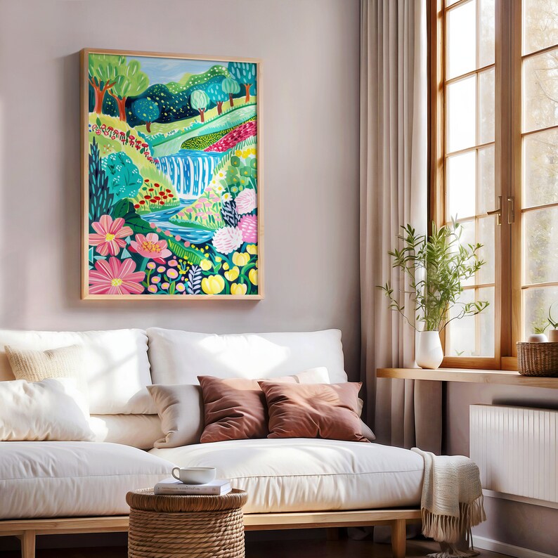 May include: A framed painting of a colorful landscape with a waterfall, flowers, and trees. The painting is in a light wood frame and is hanging on a light pink wall.