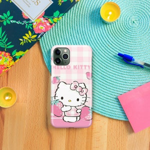 Puede incluir: Una funda de tel&eacute;fono a cuadros rosa y blancos con un dise&ntilde;o de Hello Kitty. Hello Kitty est&aacute; sosteniendo una fresa y hay fresas esparcidas a su alrededor. La funda tiene un recorte para el objetivo de la c&aacute;mara.