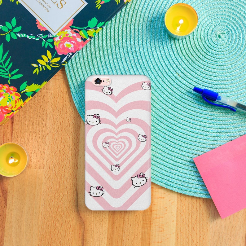 K&ouml;nnte beinhalten: Eine rosa und wei&szlig;e Handyh&uuml;lle mit einem wirbelnden Herzdesign und einem sich wiederholenden Muster von Hello Kitty-Charakteren.