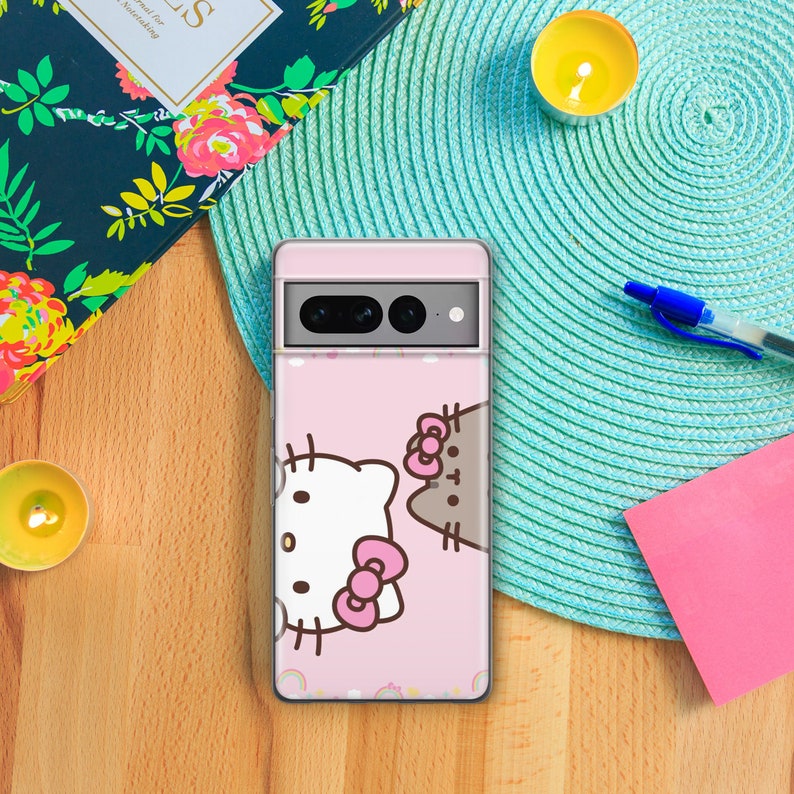 Pode incluir: Uma capa de telefone rosa com um design de Hello Kitty e um gato Pusheen. A capa tem uma parte de tr&aacute;s transparente e uma borda rosa.