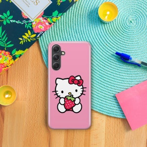 以下が含まれることがあります： ピンクの携帯電話ケースにハローキティのデザインが施されています。ハローキティは赤いイチゴを持っています。ケースには3つの穴が開いたカメラの切り抜きがあります。