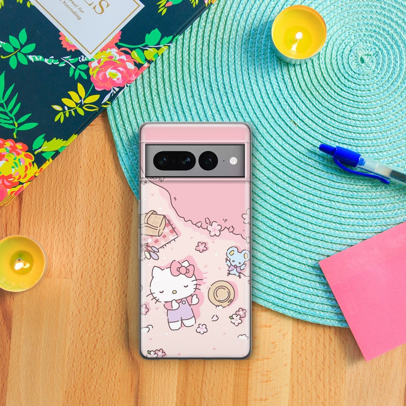 May include: A pink phone case with a Hello Kitty design. The case features Hello Kitty sitting on a pink and white floral background with a small mouse character. The case has a camera cutout and a pink border.