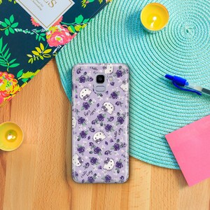 K&ouml;nnte beinhalten: Eine transparente Handyh&uuml;lle mit lila Hintergrund und einem sich wiederholenden Muster aus Hello Kitty-Figuren und lila Rosen. Der Text "Hello Kitty" und "Happy Birthday" ist auf der H&uuml;lle sichtbar.