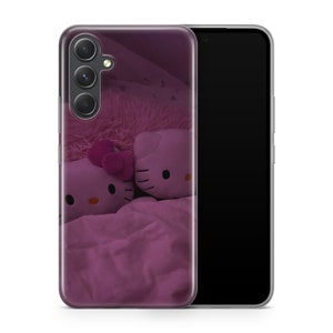 Puede incluir: Una funda transparente para tel&eacute;fono con un dise&ntilde;o rosa de Hello Kitty. La funda presenta dos personajes de Hello Kitty en una cama rosa con una manta rosa peluda. La funda tiene una pantalla de tel&eacute;fono negra en la parte posterior.