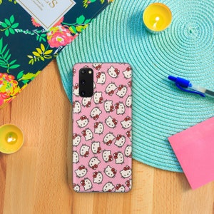 May include: A rectangular smartphone case featuring a repeating pattern of white Hello Kitty character faces with red bows on a light pink background. The case has a vertical camera cutout on the upper left side with three circular lenses.