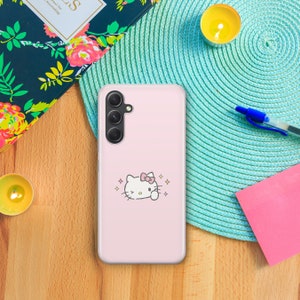 May include: A pink phone case with a white Hello Kitty design. The case has a camera cutout and a pink background.