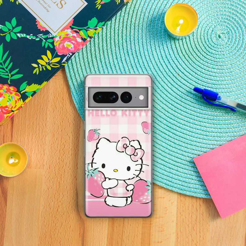 Pode incluir: Uma capa de telefone rosa e branca Hello Kitty com um padr&atilde;o xadrez e morangos. A capa tem um verso transparente e uma protuber&acirc;ncia de c&acirc;mera elevada.