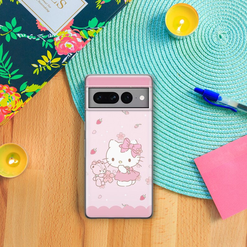May include: A pink phone case with a Hello Kitty design. Hello Kitty is holding a small teddy bear and there are pink flowers and strawberries on the case.