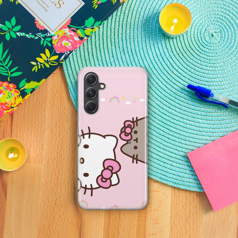 May include: A pink phone case with a Hello Kitty and a Pusheen cat design. The case has a rainbow and white clouds on it.