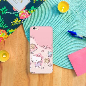 K&ouml;nnte beinhalten: Eine rosa iPhone-H&uuml;lle mit einem Hello-Kitty-Design. Die H&uuml;lle zeigt Hello Kitty und eine kleine Mausfigur auf einem rosa Hintergrund mit wei&szlig;en Blumen und einem Picknickkorb.