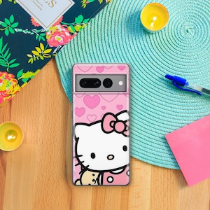 Puede incluir: Una funda transparente para tel&eacute;fono con un dise&ntilde;o rosa de Hello Kitty. La funda tiene un fondo rosa con corazones blancos y una gran ilustraci&oacute;n de Hello Kitty. Hello Kitty est&aacute; sosteniendo un peque&ntilde;o oso marr&oacute;n.