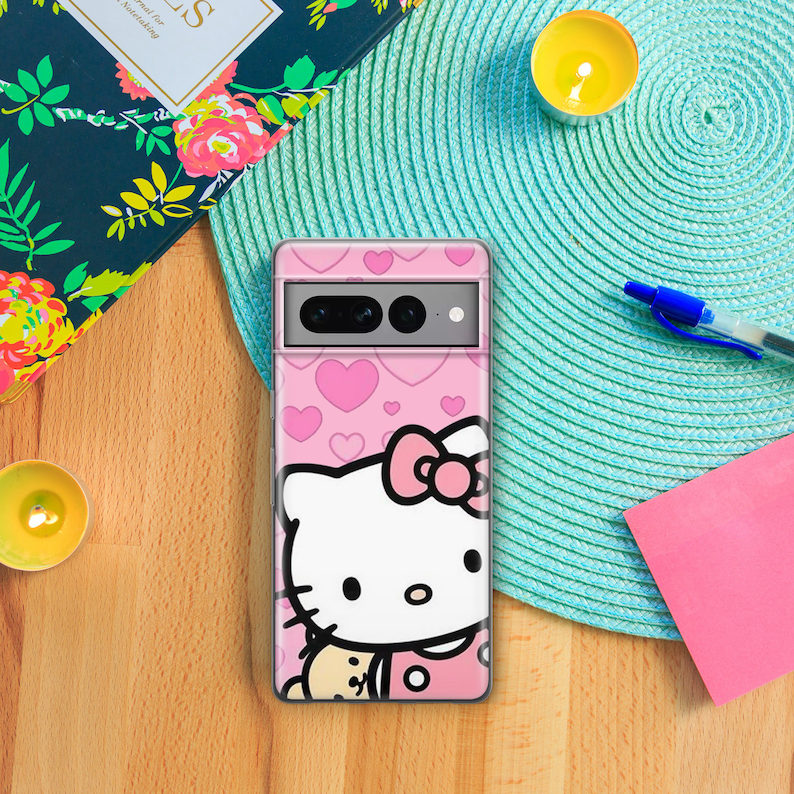Puede incluir: Una funda transparente para tel&eacute;fono con un dise&ntilde;o rosa de Hello Kitty. La funda tiene un fondo rosa con corazones blancos y una gran ilustraci&oacute;n de Hello Kitty. Hello Kitty est&aacute; sosteniendo un peque&ntilde;o oso marr&oacute;n.