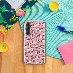 Op de afbeelding: Een roze telefoonhoesje met een herhalend patroon van Hello Kitty-gezichten. Het hoesje heeft een camera-uitsparing en een zwarte camera lens.