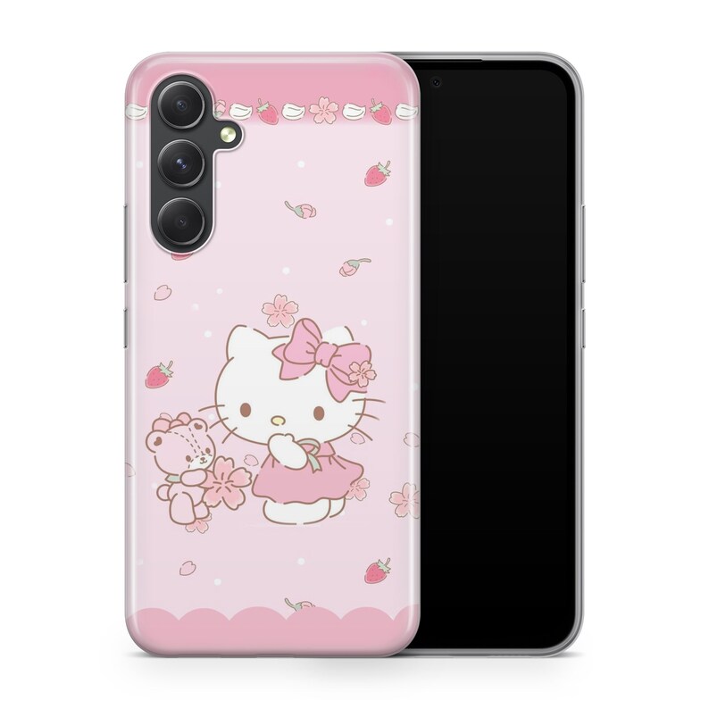May include: A light pink smartphone case featuring a graphic of Hello Kitty wearing a pink bow and dress, standing next to a small teddy bear. The design includes scattered pink cherry blossoms, small red strawberries, and white polka dots.