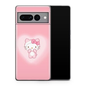 以下が含まれることがあります： ピンクの電話ケースに、ピクセルアートのハローキティのデザインが施されています。ケースは背面が透明で、前面はピンクで、白いハローキティがピンクのリボンをつけています。