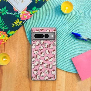 Op de afbeelding: Een transparante telefoonhoes met een roze achtergrond en een herhalend patroon van Hello Kitty-figuren. De hoes heeft een zwarte camera-uitsparing.