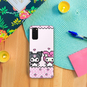 Puede incluir: Una funda de tel&eacute;fono rosa y blanca con un dise&ntilde;o pixelado de Hello Kitty y un personaje blanco y negro con un lazo. La funda tiene un patr&oacute;n de cuadros rosa y blanco con fresas.