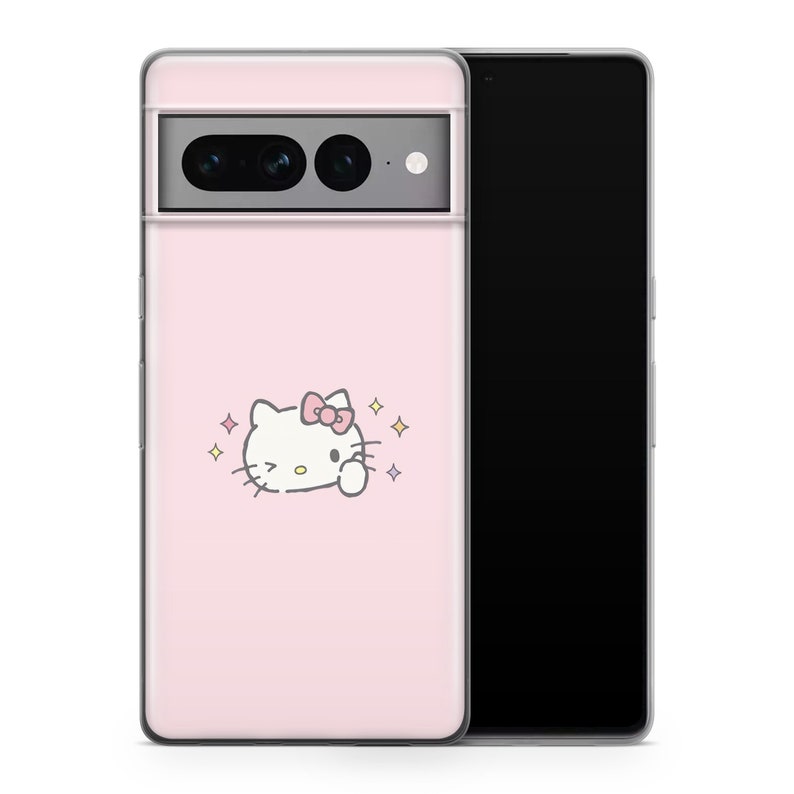 以下が含まれることがあります： ピンクの携帯電話ケースに、白いハローキティのイラストとピンクのリボンが描かれています。ケースは背面が透明で、前面が黒です。