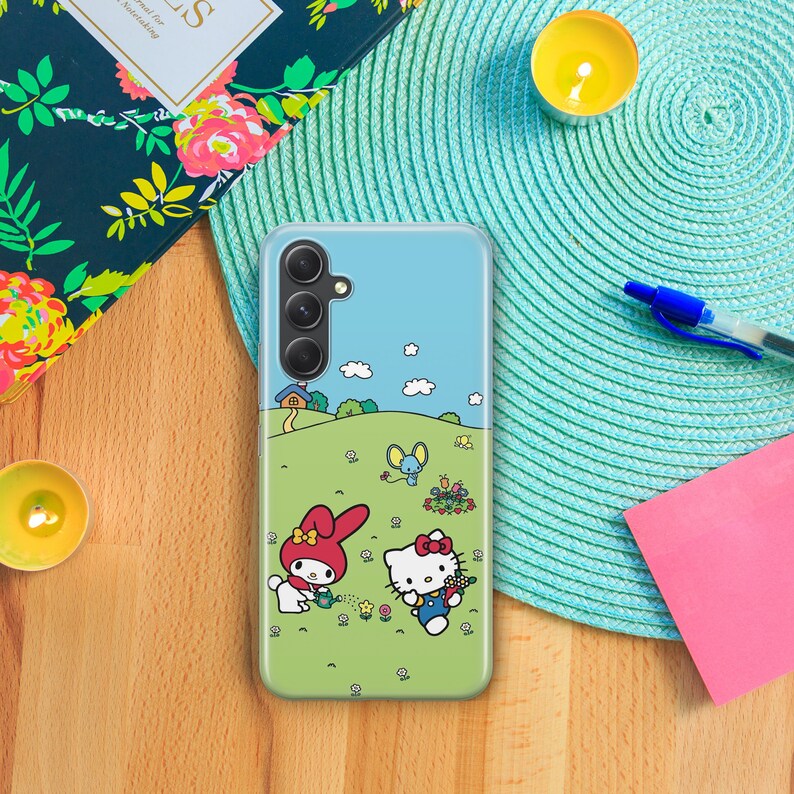 May include: A clear phone case with a blue background and a cartoon image of Hello Kitty and My Melody. The case has a camera cutout and a white border.