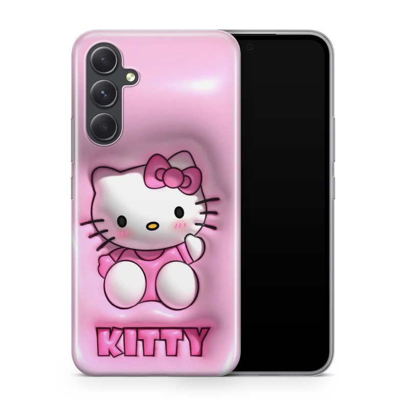 Puede incluir: Una funda de tel&eacute;fono rosa con un dise&ntilde;o de Hello Kitty en 3D. La funda tiene un recorte para el objetivo de la c&aacute;mara y el texto "KITTY" impreso en la parte inferior.