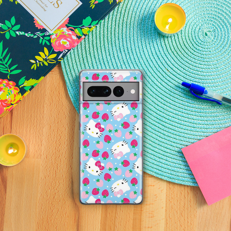 K&ouml;nnte beinhalten: Eine transparente Handyh&uuml;lle mit blauem Hintergrund und einem Muster aus wei&szlig;en Hello-Kitty-Figuren und rosa Erdbeeren.
