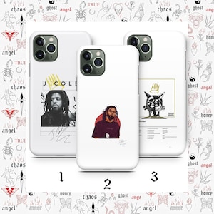 Peut inclure: Trois coques d'iPhone blanches avec des designs différents. La première coque présente une photo en noir et blanc de J. Cole avec sa signature. La deuxième coque présente une photo en noir et blanc de J. Cole avec un cercle rouge derrière lui. La troisième coque présente une illustration en noir et blanc d'une couronne avec un visage dessus. Le texte "Sinner" est imprimé sur la coque.