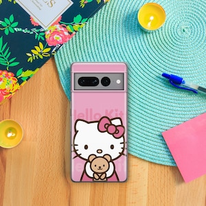 Puede incluir: Una funda de tel&eacute;fono rosa con un dise&ntilde;o de Hello Kitty. Hello Kitty est&aacute; sosteniendo un oso de peluche marr&oacute;n. La funda tiene un recorte para la c&aacute;mara y un fondo rosa.