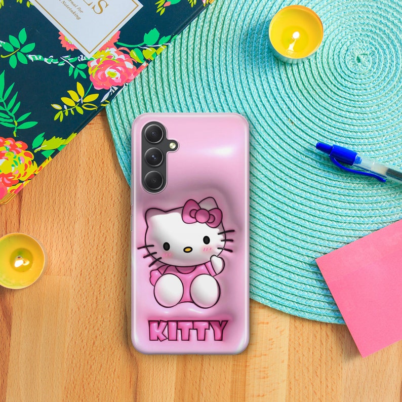Puede incluir: Una funda de tel&eacute;fono rosa con un dise&ntilde;o de Hello Kitty en 3D. La funda tiene una figura de Hello Kitty en relieve con un lazo rosa y un vestido rosa. La funda tambi&eacute;n tiene la palabra "KITTY" impresa en la parte inferior.